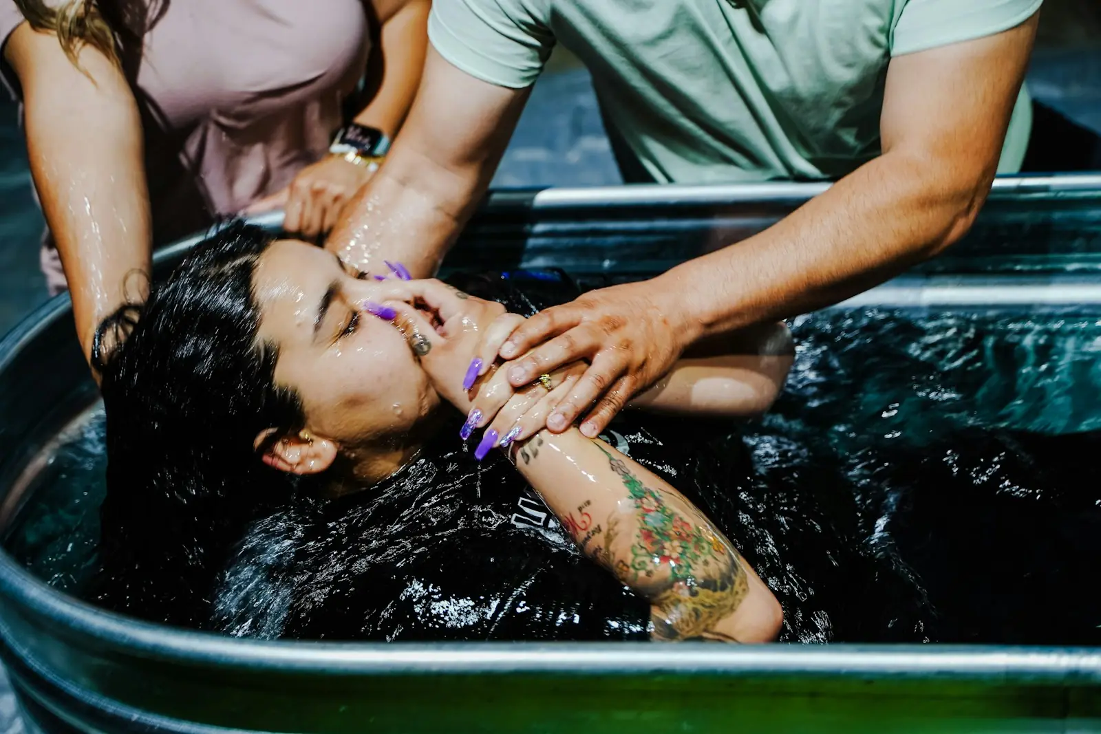 A woman being baptized, eyes closed, water on her face